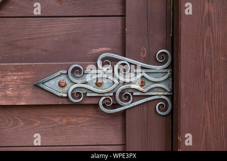 Close-up su una decorazione a cerniera forgiato in stile antico con una configurazione attorcigliata su un marrone porta di legno. Costruzione e decorazione di edifici. Foto Stock