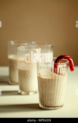 Tradizionale winter in casa gustosi cocktail di Natale zabaione con latte,rum, cannella e noce moscata decorate candy cane su sfondo bianco con ombra Foto Stock