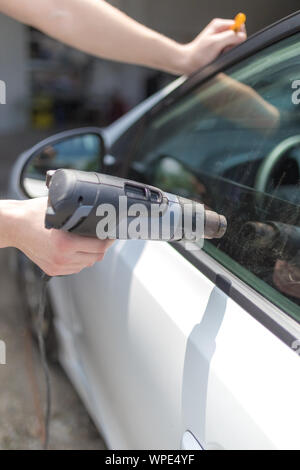 Lavoratore rimozione auto finestra foglio di pellicola utilizzando la pistola ad aria calda. Foto Stock