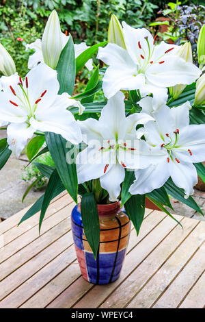 Un mazzetto di gigli bianchi disposti in un vaso colorato su un di legno Tavolo da giardino, London, Regno Unito Foto Stock