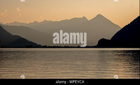 Tramonto guardando verso il lago di Brienz in Svizzera. Le alte montagne cast una silhouette contro il cielo arancione e riflessi nell'acqua del Foto Stock