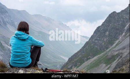 Un solitario escursionista femmina si affaccia su alcune delle vette alpine e valle. Aria di tempesta sulle alte cime come ella medita i panorami della valle. Foto Stock