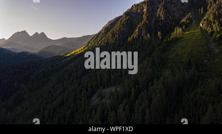 Antenna fuco viste di un verde lussureggiante vallata alpina e le vette circostanti la balneazione nella luce del sole in una mattina presto drone di volo. Foto Stock