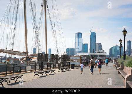 New York City waterfront, vista in estate di persone a piedi lungo il Battery Park Esplanade di Lower Manhattan, New York City, Stati Uniti d'America Foto Stock