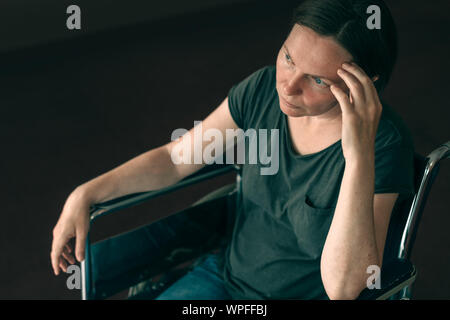 Premuto triste donna in sedia a rotelle usurati guardando fuori dalla finestra e pensare, lonely disabile adulto persona caucasici in ambienti interni Foto Stock