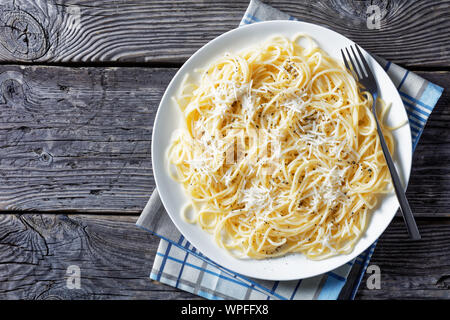 Spaghetti mescolato con formaggio pecorino grattugiato e spolverata di pepe nero macinato fresco su una piastra bianca con una forcella, cacio e pepe, cucina italiana, v Foto Stock