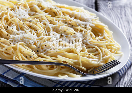 Close-up di cacio e pepe, cremosa spaghetti cacio e pepe nero su una piastra bianca su un vecchio tavolo in legno, cucina italiana, vista da sopra, ma Foto Stock