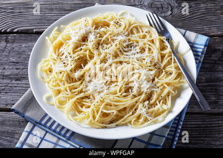 Cremosa di spaghetti con formaggio e spolverata di pepe nero macinato su una piastra bianca su un vecchio tavolo di legno, cacio e pepe, cucina italiana, vista da ab Foto Stock