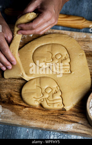 Primo piano di un giovane uomo caucasico preparare qualche cranio-cookie sagomato per Hallowen, sul grigio di una tavola in legno rustico Foto Stock