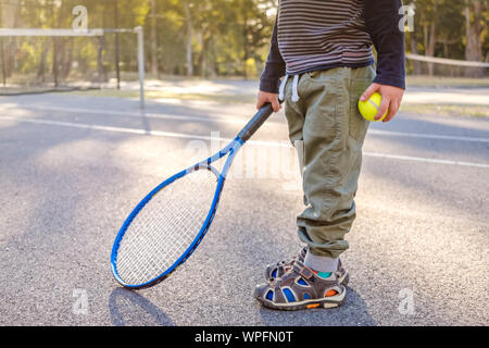 Piccolo Ragazzo australiano con la racchetta e la palla al campo da tennis esterno in Australia in un giorno Foto Stock