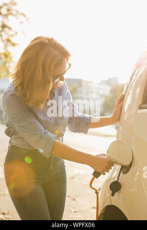 Giovane donna è in carica carsharing auto elettrica. Foto Stock