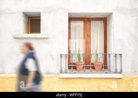 Vecchia donna camminare per la strada in Andalusia, Spagna contro un balcone decorato con vasi da fiori e gerani. Svuotare lo spazio di copia per l'editor di testo. Foto Stock