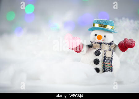 Un pupazzo di neve e un mini cuscino a cuore su sfondo bokeh, con spazio per le copie per il saluto stagionale. buon natale o felice anno nuovo, selezione AF Point, Classe Foto Stock