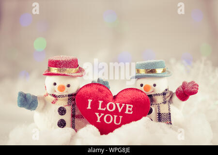 Un pupazzo di neve e un mini cuscino a cuore su sfondo bokeh, con spazio per le copie per il saluto stagionale. buon natale o felice anno nuovo, selezione AF Point. Vinta Foto Stock