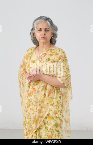 Senior woman standing with her hands clasped and looking sad Stock Photo