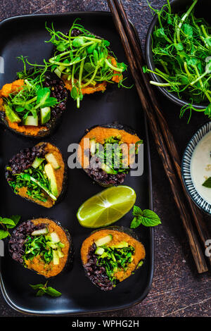 Vegano rotoli di sushi con riso nero, avocado e la patata dolce su un piatto nero, vista dall'alto. Cibo Vegan concetto. Foto Stock