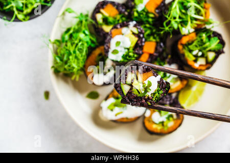 Vegano rotoli di sushi con riso nero, avocado e patate dolci su una piastra bianca. Cibo Vegan concetto. Foto Stock