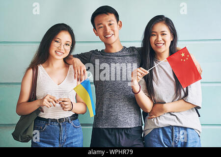 Gruppo di tre felice cinese internazionale di studenti asiatici sorridente e tenendo le bandiere di Cina e Ucraina in università Foto Stock