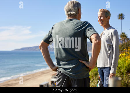 Felice coppia senior parlando su cliff beach contro sky durante la giornata di sole Foto Stock