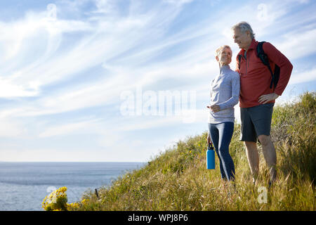 Sorridente coppia senior permanente sulla scogliera dal mare contro sky Foto Stock