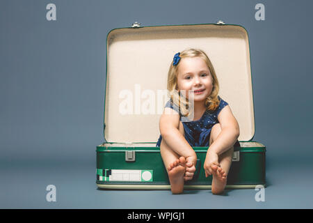 Ritratto di un bambino di 3 anni ragazza seduta a piedi nudi all'interno di una vecchia valigia. shot presi in studio. Foto Stock