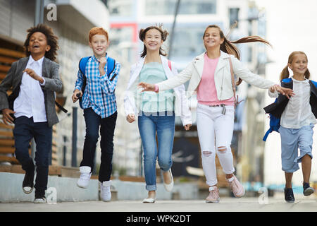 Gruppo di bambini felici in abbigliamento casual sorridente e correndo insieme nella città all'aperto Foto Stock