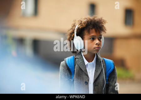 African scolaro con zaino indossando le cuffie e ascoltare musica mentre si cammina lungo la strada Foto Stock