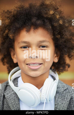 Ritratto di Allegro ragazzo africano con i capelli ricci e con le cuffie intorno al suo collo sorridente in telecamera Foto Stock