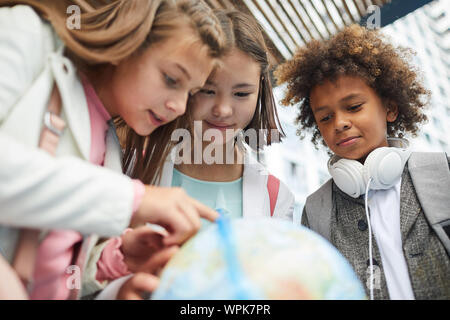 Gruppo di multietnica studenti elementari ricerca insieme diversi luoghi interessanti sul globo Foto Stock