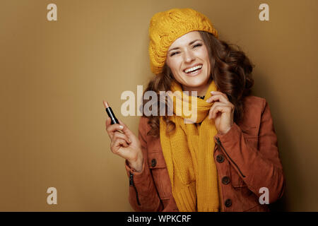 Ciao autunno. Ritratto di felice donna moderna in giallo berretto e sciarpa con igienico di rossetto contro lo sfondo di bronzo. Foto Stock