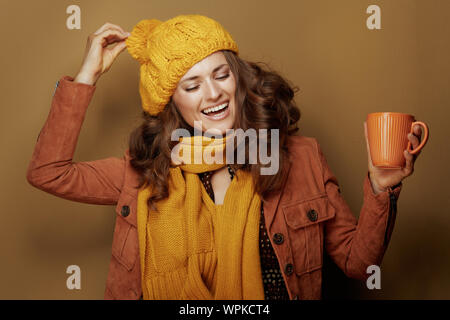 Ciao autunno. allegro giovane donna in giallo berretto e sciarpa con tazza di zucca latte isolate su beige. Foto Stock