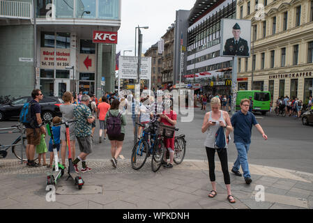 Turisti a Checkpoint Charlie, Berlino, con il ritratto dell'ex sergente statunitense Jeff Harper ritratto sullo sfondo. Foto Stock