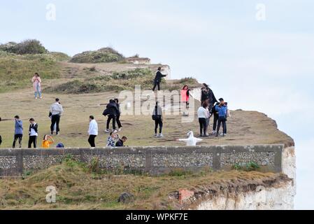 Giovani turisti coreani scattare fotografie in piedi sul bordo di chalk scogliere a Birling Gap Eastbourne East Sussex England Regno Unito Foto Stock