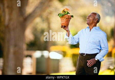 Senior uomo tendente al suo piante in vaso in giardino. Foto Stock