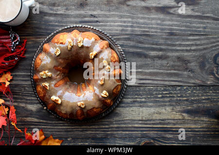Deliziosi, zucca Spice Bundt Cake satinato marrone con glassa di zucchero e noci con foglie di autunno e caffè su una tavola in legno rustico sfondo. Foto Stock