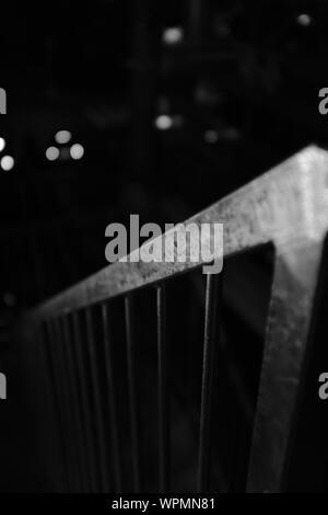 Immagine in scala di grigi selettiva verticale di una ringhiera in acciaio su sfondo nero sfocato Foto Stock