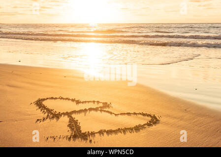 Il giorno di San Valentino di sunny beach. Due cuori attirato in sabbia, concetto di amore Foto Stock