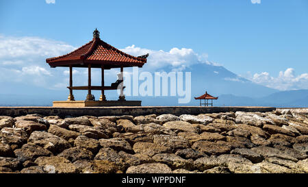 Silhouette di uomo in pieno giorno di prendere un periodo di riposo in ombra sotto un rifugio tradizionale sulla spiaggia di Sanur, Bali, Indonesia. Foto Stock