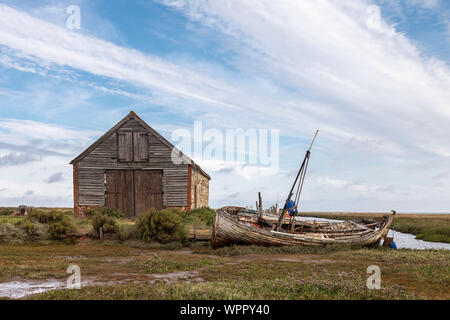 Una immagine di un vecchio fienile di carbone e la barca da pesca su una via navigabile che illustra i giorni passati a Thornham Norfolk, Inghilterra, Regno Unito. Foto Stock