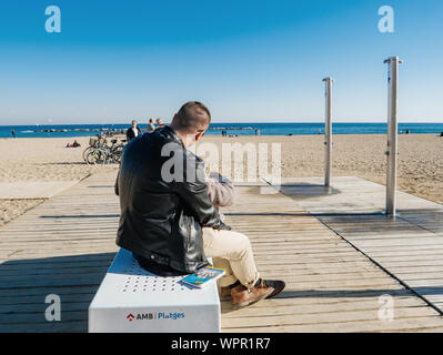 Barcellona, Spagna - Nov 11, 2017: giovane appoggiato su di una spiaggia di Barceloneta sedia ammirando il mare calmo Foto Stock