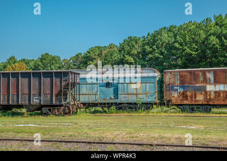 La formazione di ruggine e decadenti railroad boxcars e una tramoggia lasciati abbandonati sui binari in un campo incolto in una giornata di sole in estate Foto Stock