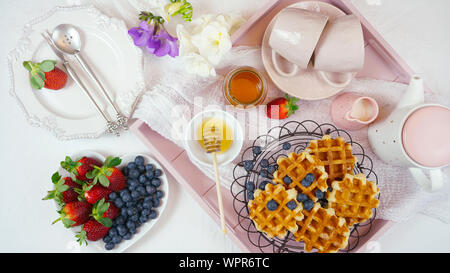 Moderno blush rosa vassoio colazione con cialde, miele e frutta. Foto Stock