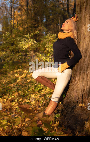 La ragazza poggia su un albero e viene fotografata al tramonto in abiti da cowboy, stivali marroni piede su un albero Foto Stock