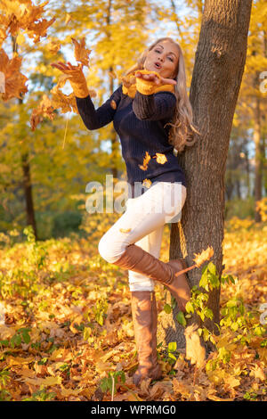 La ragazza poggia su un albero e viene fotografata al tramonto in abiti da cowboy, stivali marroni Foto Stock