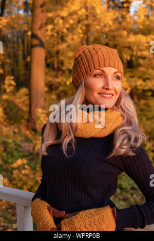 In autunno, una donna si alza e ci guarda non belle foglie nella foresta, è in un cappello e in una sciarpa. Capelli sciolti nelle mani dei mittens Foto Stock