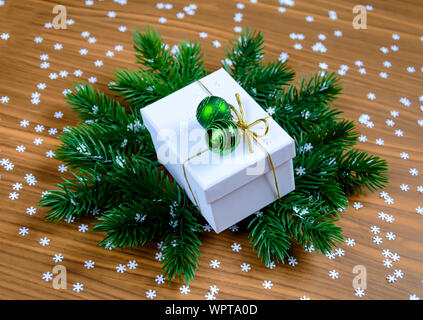 Elegante bianco Natale confezione regalo con verde baubles su Abete rami e lo sfondo di legno Foto Stock