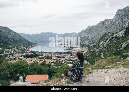 Una ragazza in solitudine si trova sulla cima di una collina o di una montagna e guarda a una splendida vista della Baia di Kotor in Montenegro. Foto Stock