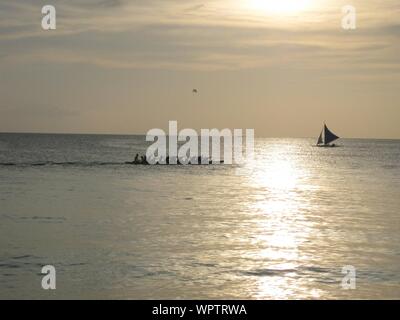Silhouette di longboat con persone che navigano sull'acqua con un cielo nuvoloso sullo sfondo Foto Stock