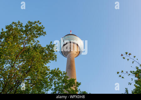 Rheinturm, alto-aumento della radio o della televisione torre circolare con la piattaforma di osservazione sulla parte superiore su treetop contro il cielo blu. Foto Stock