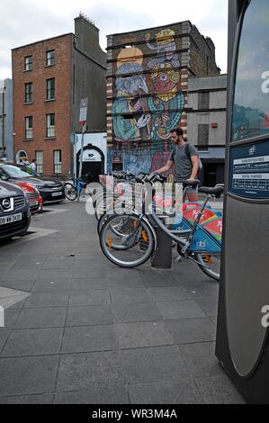 Un uomo restituisce una bicicletta per una docking station in una fila di solo mangiare sponsorizzato biciclette a Dublino a Dublino, Irlanda Foto Stock